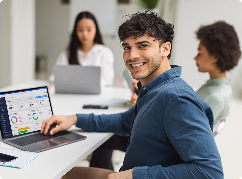 A smiling customer support representative using a laptop to demonstrate a facility management dashboard to a collaborative team.