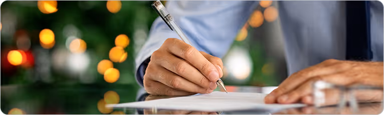 Close-up of a businessman's hand signing a legal document or contract with a pen on a desk.