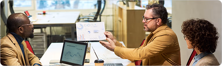 Diverse business team having a meeting in a modern office, with a man presenting data charts to colleagues.