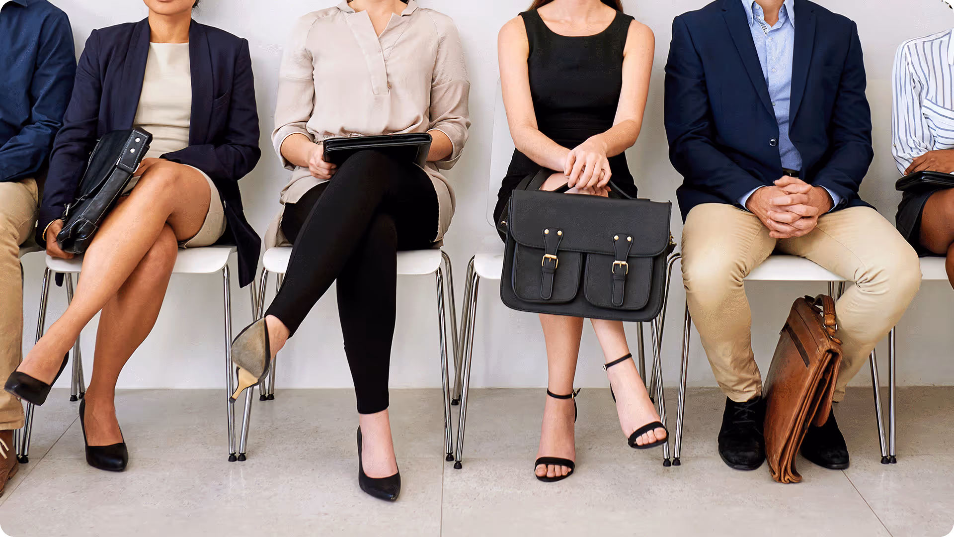 A row of job candidates sitting in a waiting room, holding bags and portfolios while waiting for a professional interview.