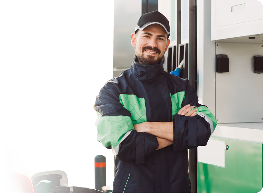 A friendly gas station worker in a navy and lime green uniform standing with arms crossed in front of a fuel pump, representing the national retail fuel industry.