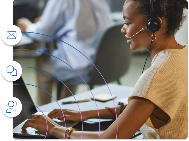 Woman wearing a headset and smiling while typing on a laptop in an office setting.