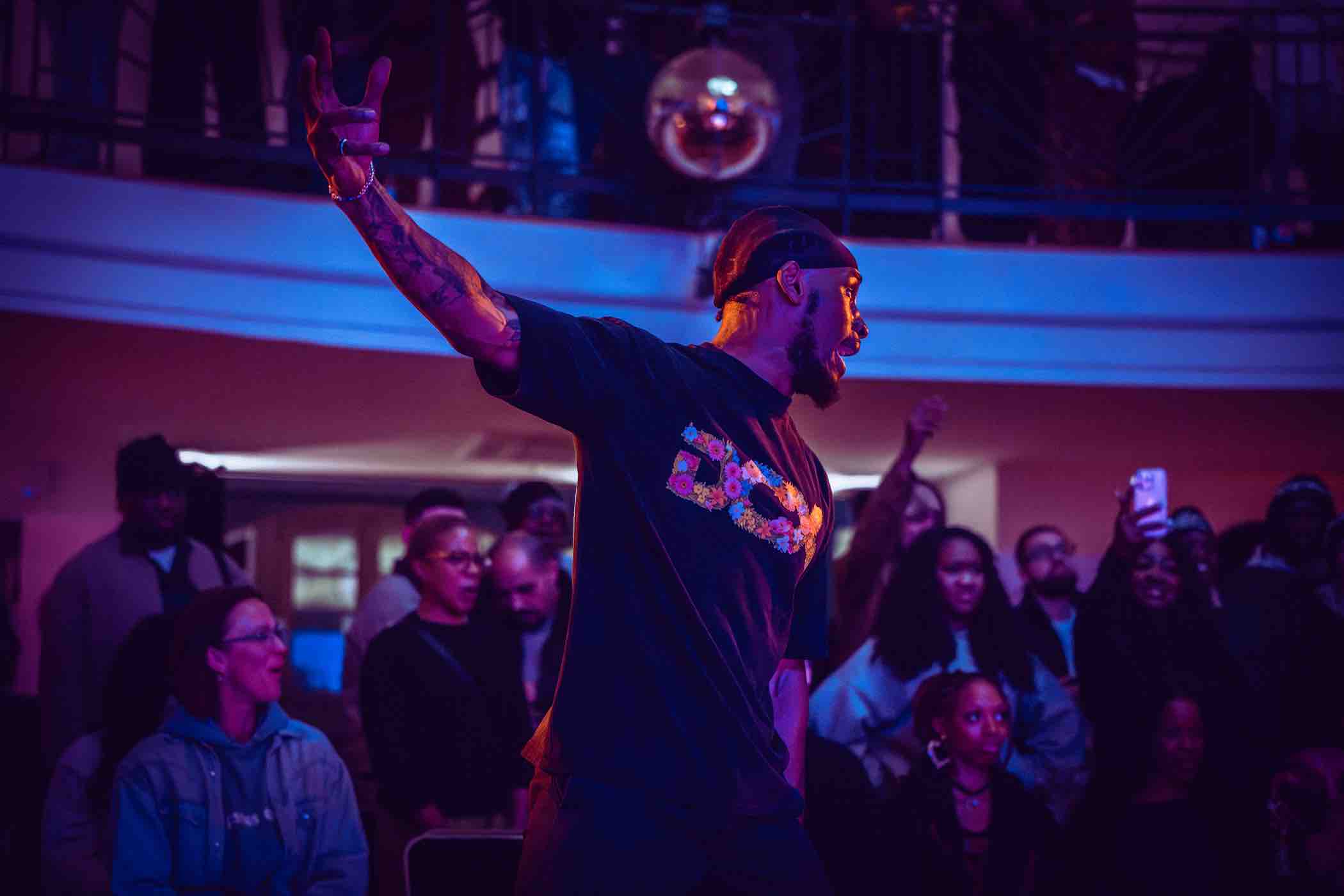 Man with tattoos and a bandana passionately performing on stage in front of an engaged audience.
