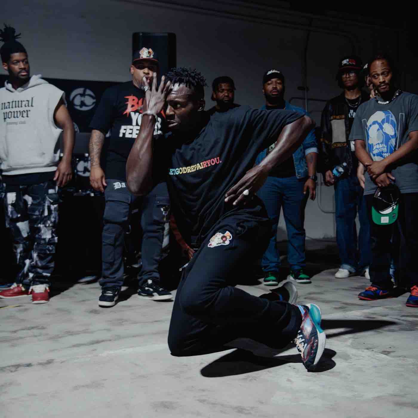Smiling young man with dreadlocks wearing a green hoodie featuring a yellow geometric tiger design.