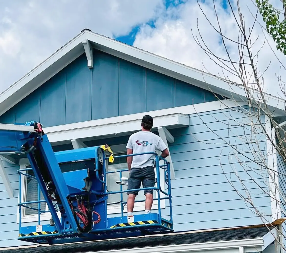 Professional exterior house painting in Billings Montana with painter on lift applying blue siding finish