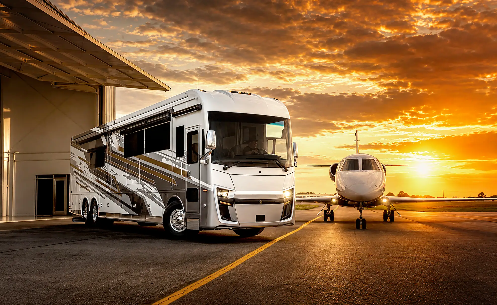 Luxury motorhome parked near a private jet on an airstrip at sunset with dramatic clouds.