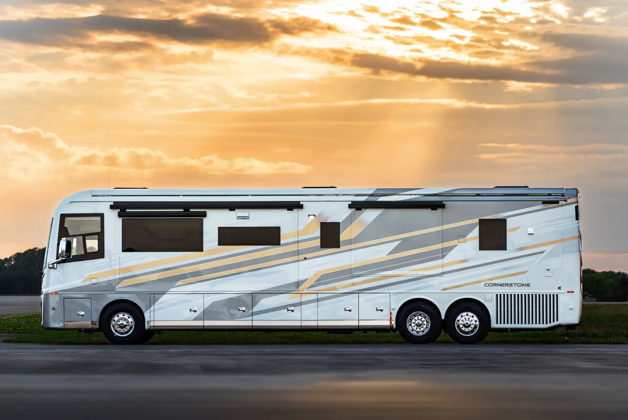 White and gray Cornerstone motorhome with yellow accents parked at sunset with cloudy sky.