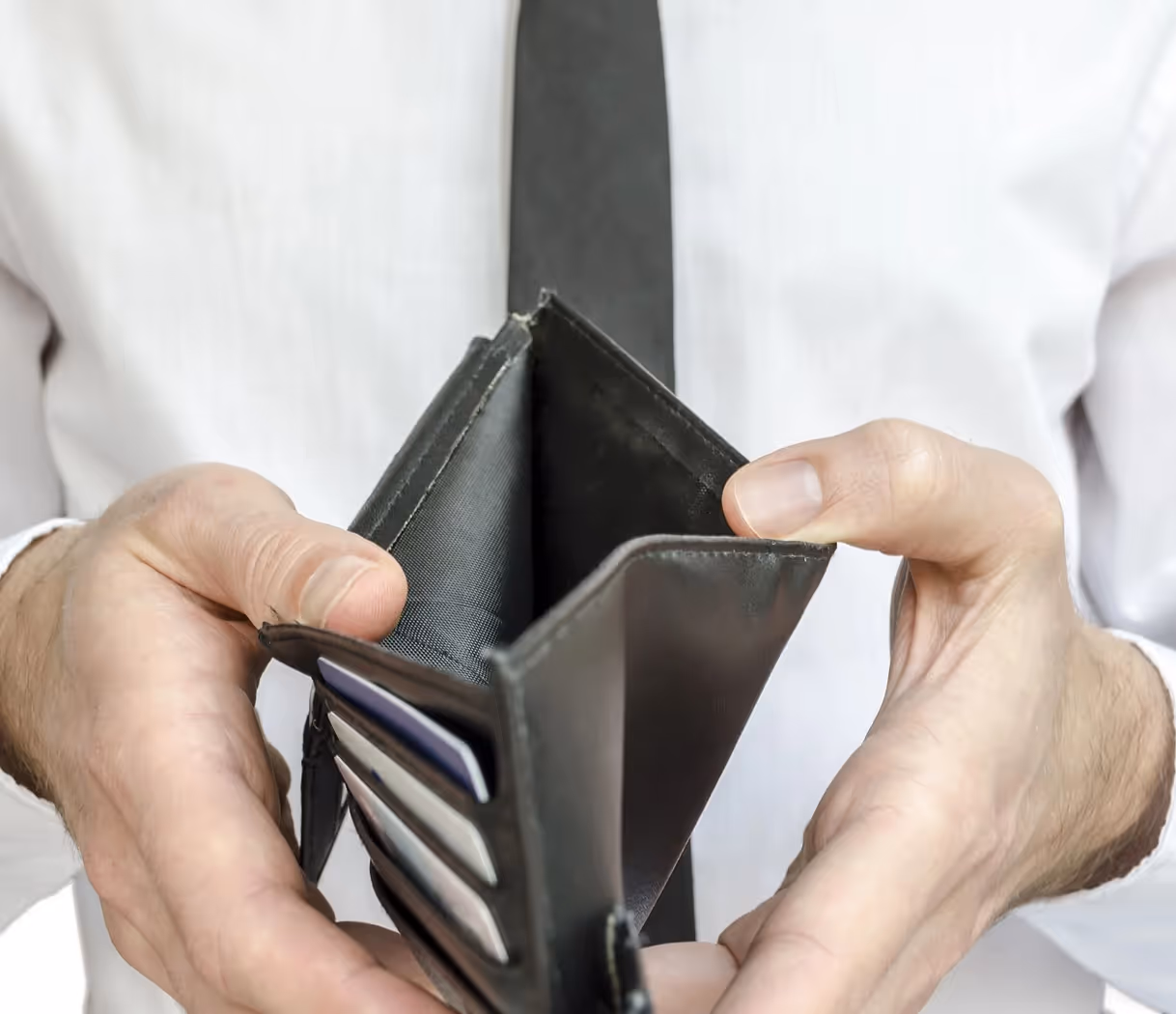 Man in white shirt and black tie holding an empty black wallet open.