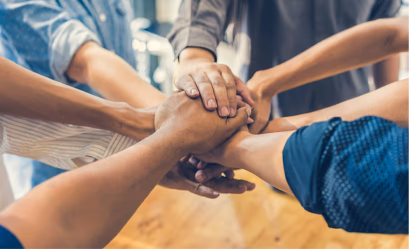 Group of people standing in a circle with their hands stacked together in a show of unity.