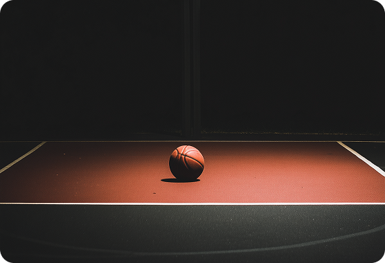 Basketball placed on the center of a dimly lit basketball court with dark surroundings.