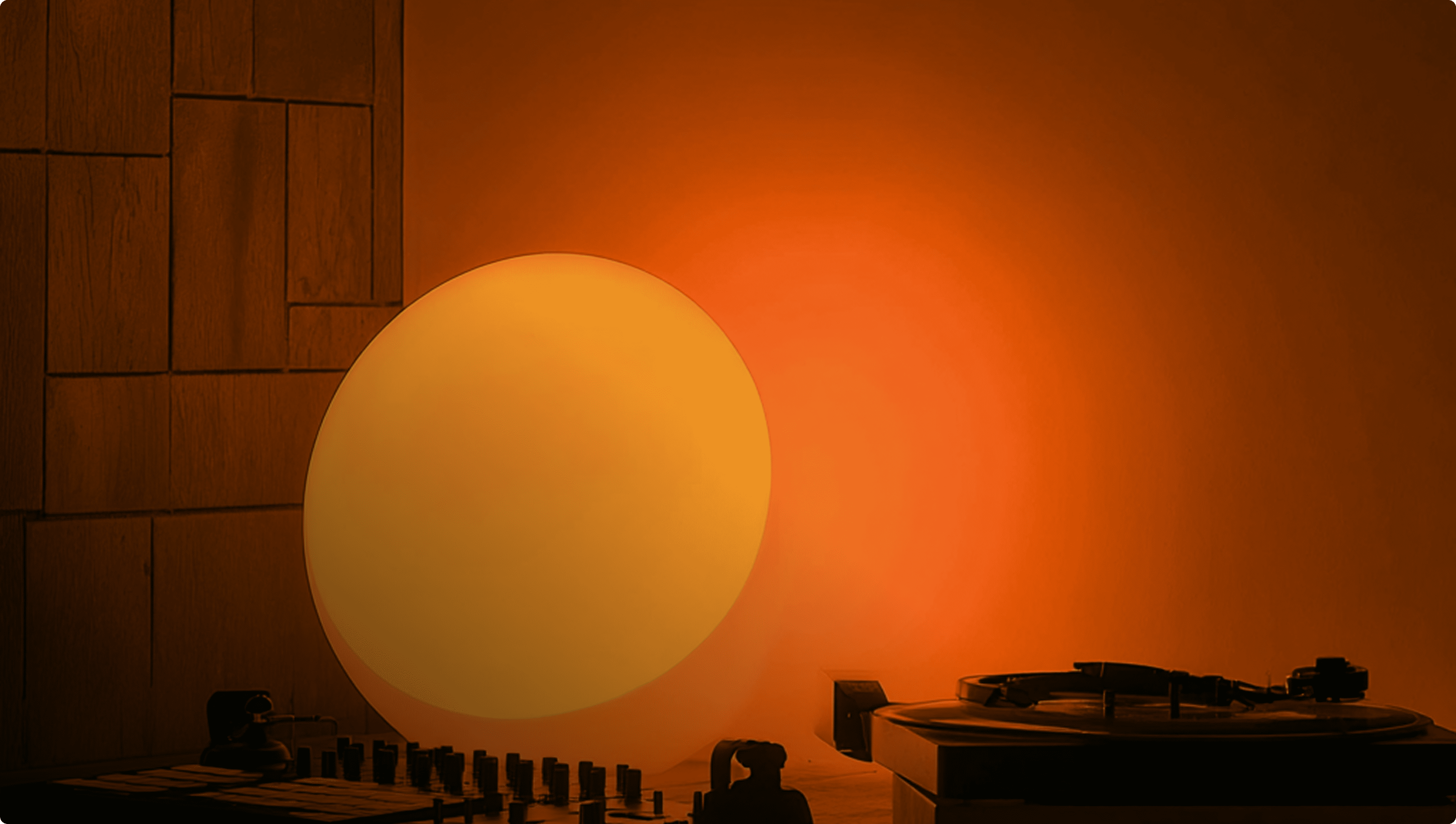 Warm orange ambient light illuminating a turntable and audio mixer on a wooden table.