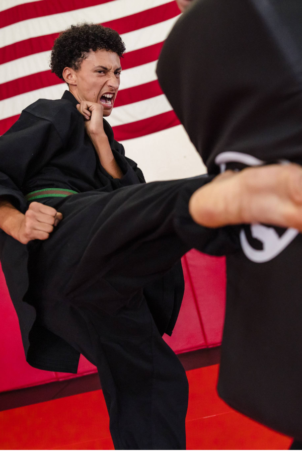 A young karate student wearing a purple belt practices a block position in karate class.