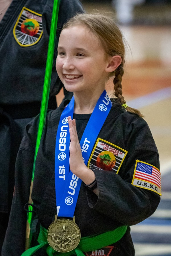 A young karate student wearing a purple belt practices a block position in karate class.