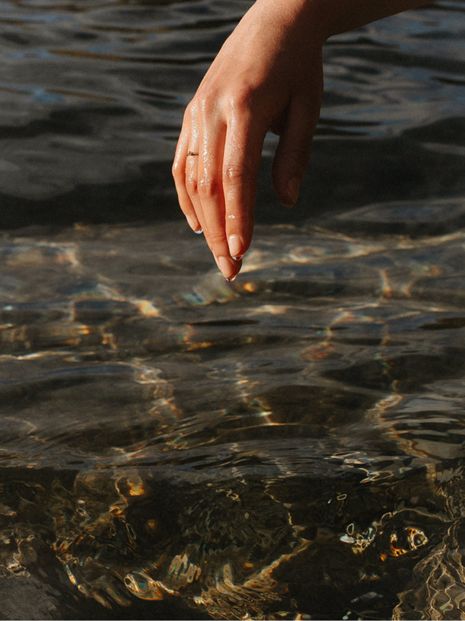 Hand gently touching the surface of rippling water with sunlight reflections.