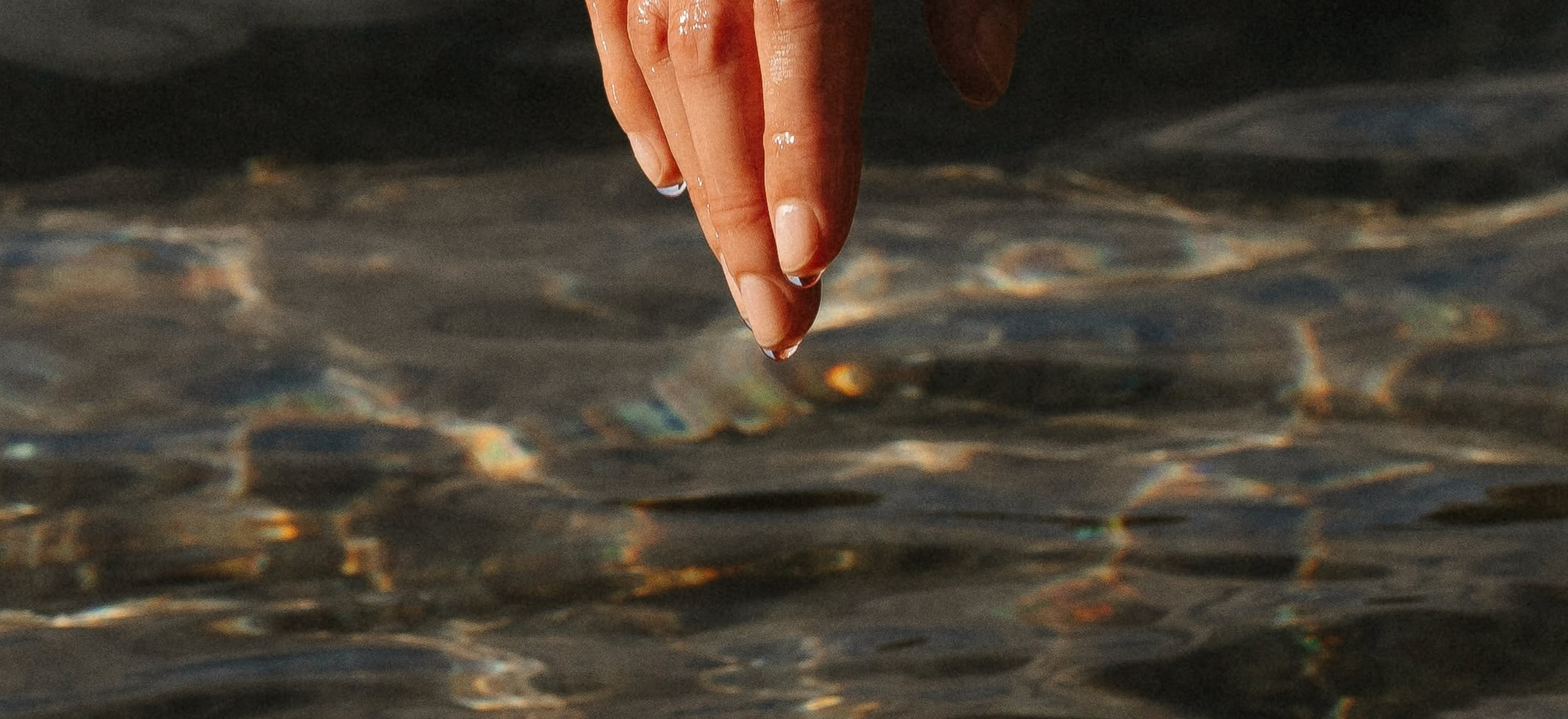Fingers gently touching the surface of water with drops falling from the hand.