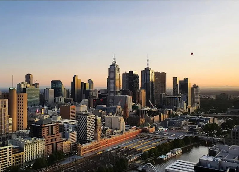 City skyline at sunset with tall buildings and a hot air balloon in the sky.