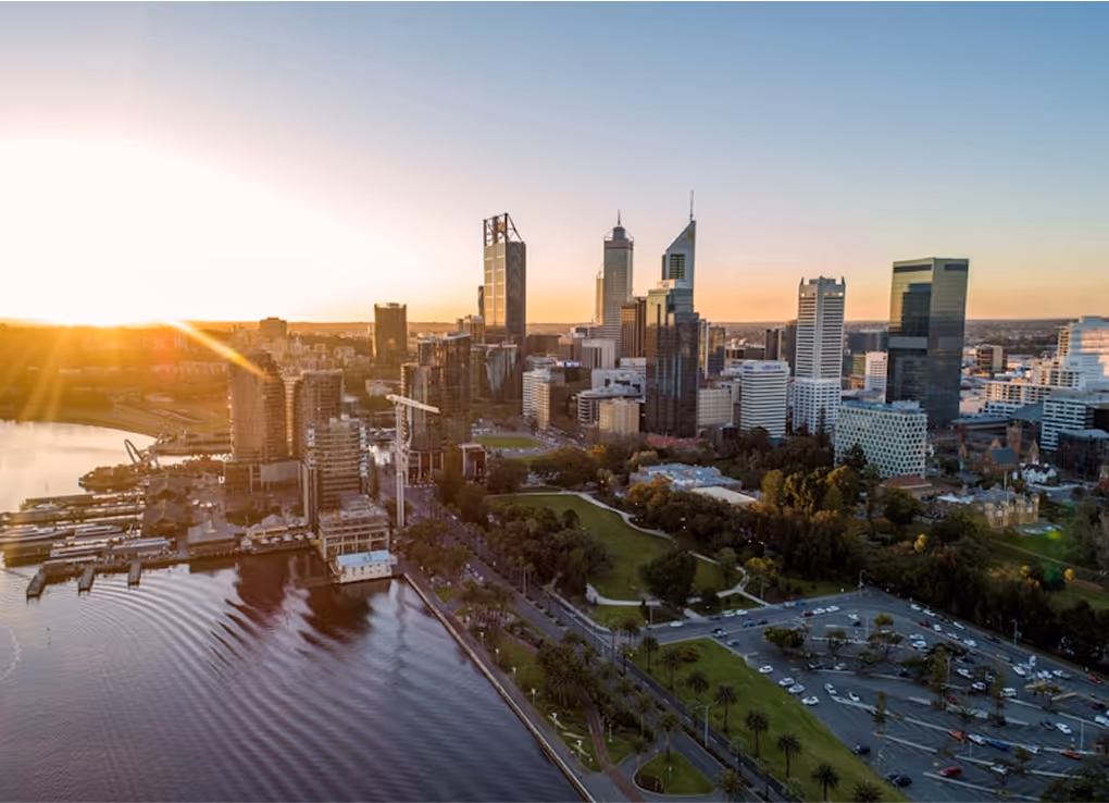 Sunset view over a city skyline with high-rise buildings, riverfront, and green parks.