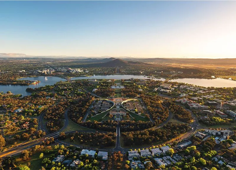 Aerial view of a planned city area with symmetrical buildings, green spaces, lakes, and surrounding residential neighborhoods at sunset.