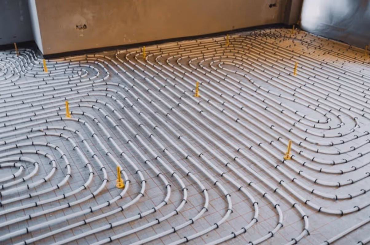 Underfloor radiant heating system installation with white pipes arranged in a looping pattern over a grid on the floor.