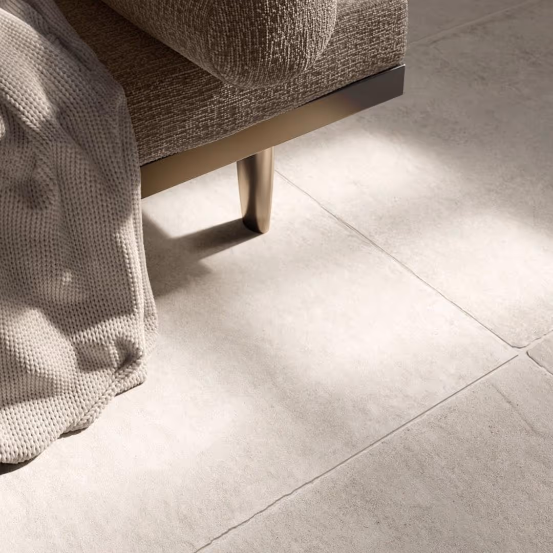 Close-up of beige textured sofa leg on light grey tiled floor with beige knitted throw draped over sofa in modern interior.