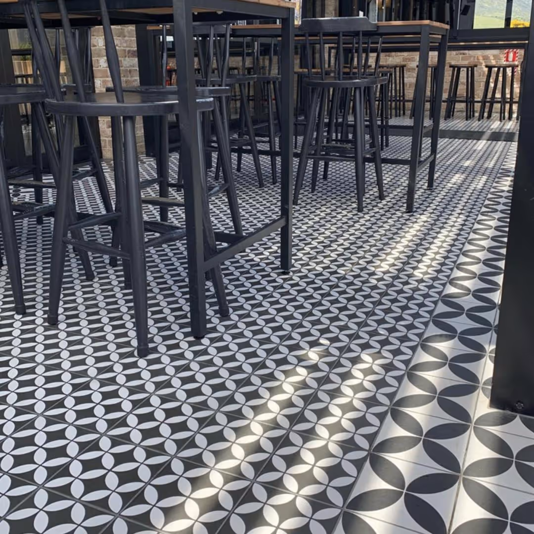 Black and white geometric patterned floor tiles in dining area with black high chairs and tables in modern interior design.