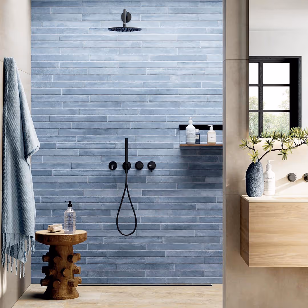 Modern bathroom shower with matte black fixtures, blue-grey subway tile walls, wooden stool with soap, and vanity with vase and soap dispenser in contemporary bathroom design.
