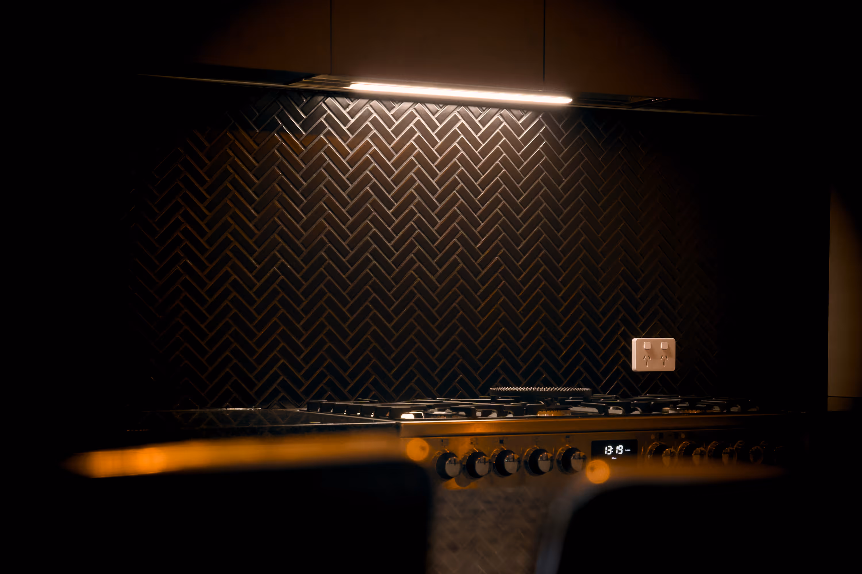 Modern kitchen stove with illuminated black herringbone tile backsplash and black range hood lighting in contemporary kitchen.