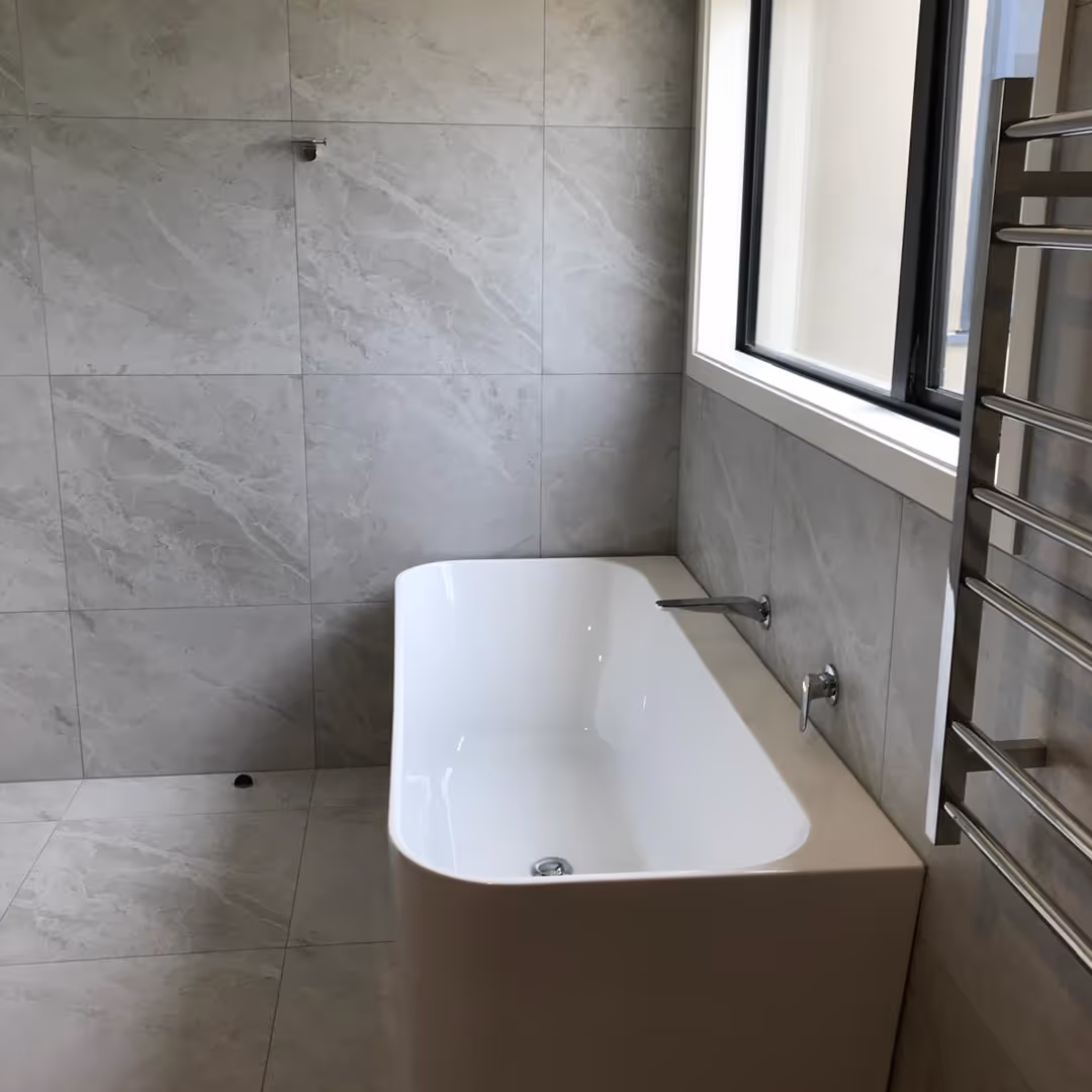 Modern bathroom with a white freestanding tub, gray marble tiles, a window, and a towel rack.