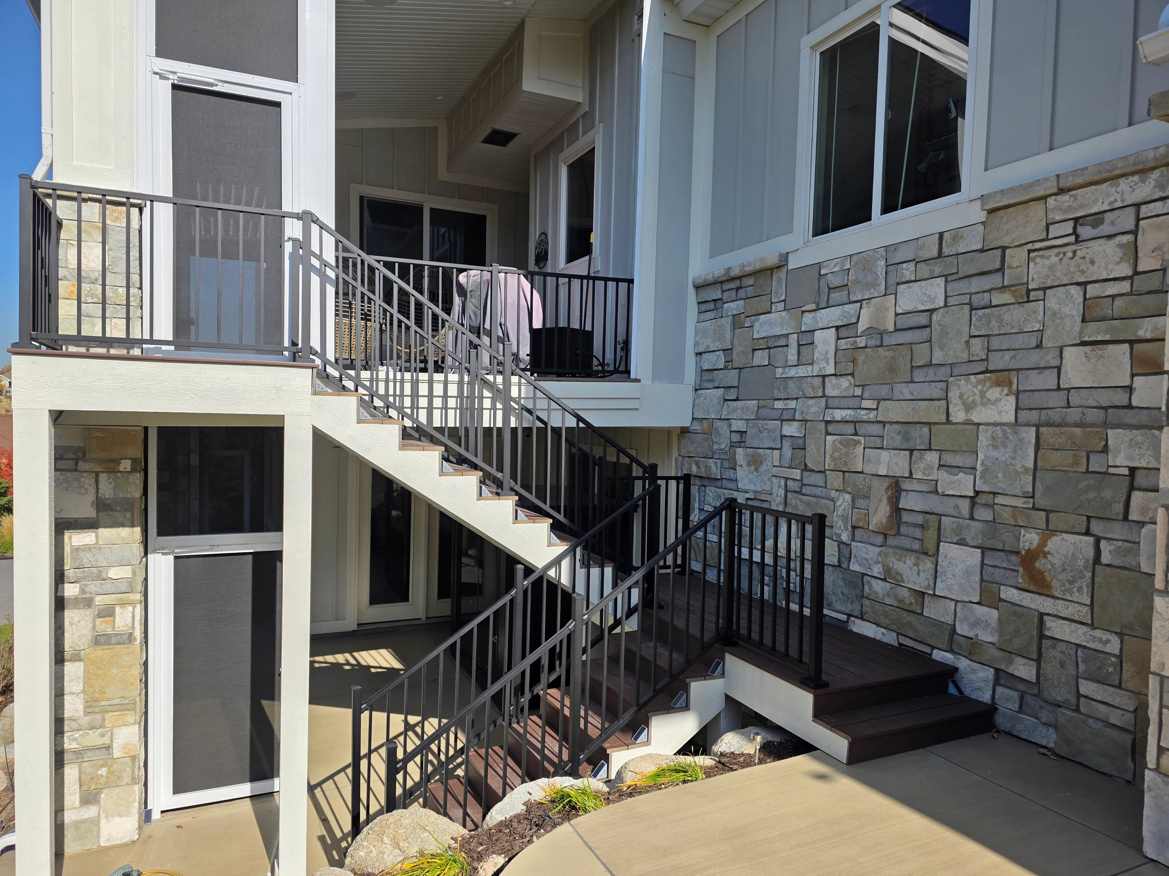 An exterior view of a home in Saratoga Springs featuring a custom upper deck and a staircase with built-in step lights and modern black aluminum railings.