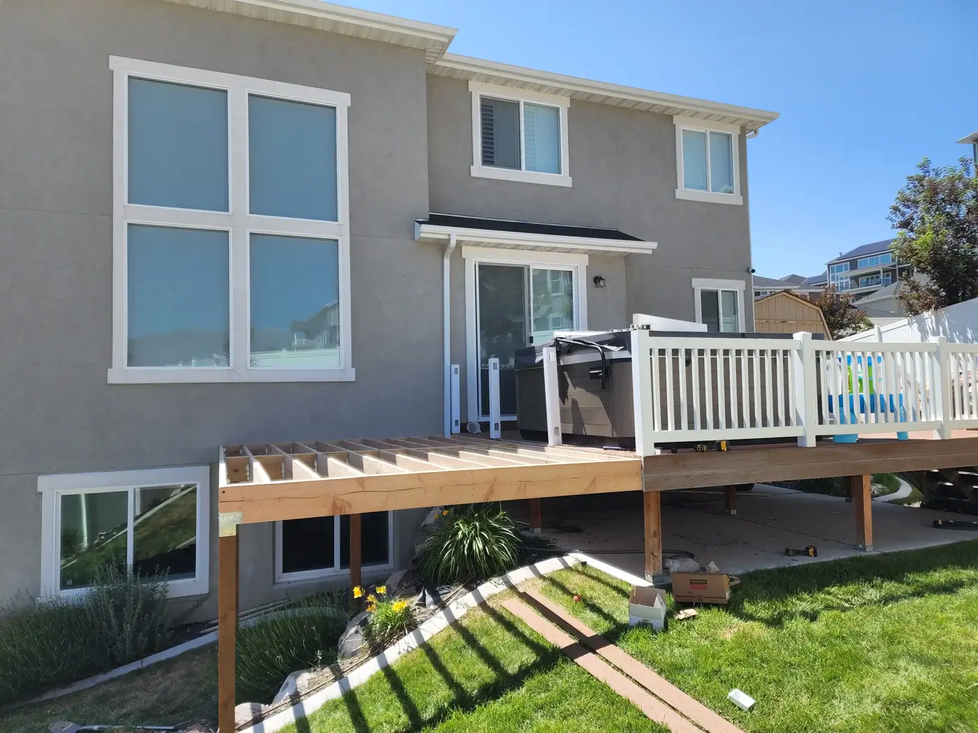 New deck addition being framed with joists beside an existing composite deck with white railing and a hot tub