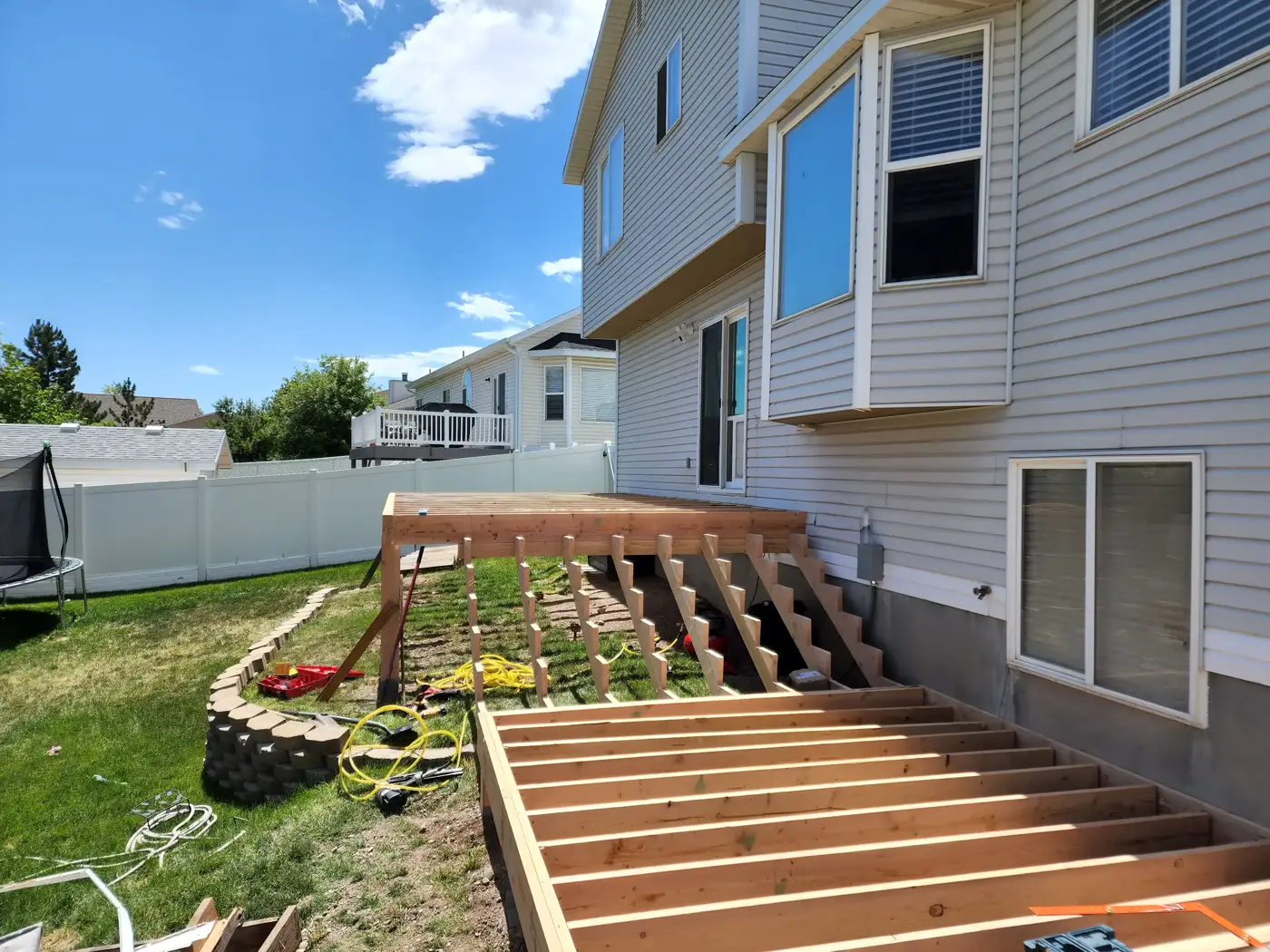 Elevated deck framing with joists and stair stringers under construction behind a two-story home