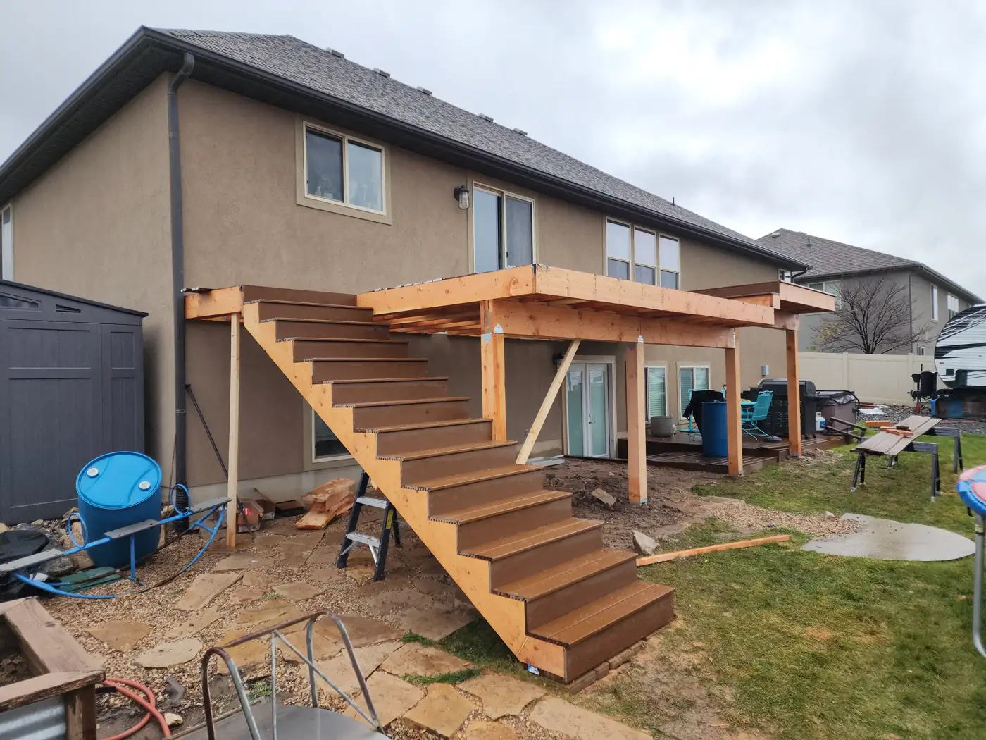 Elevated deck frame with wide timber stairs under construction at the back of a stucco home