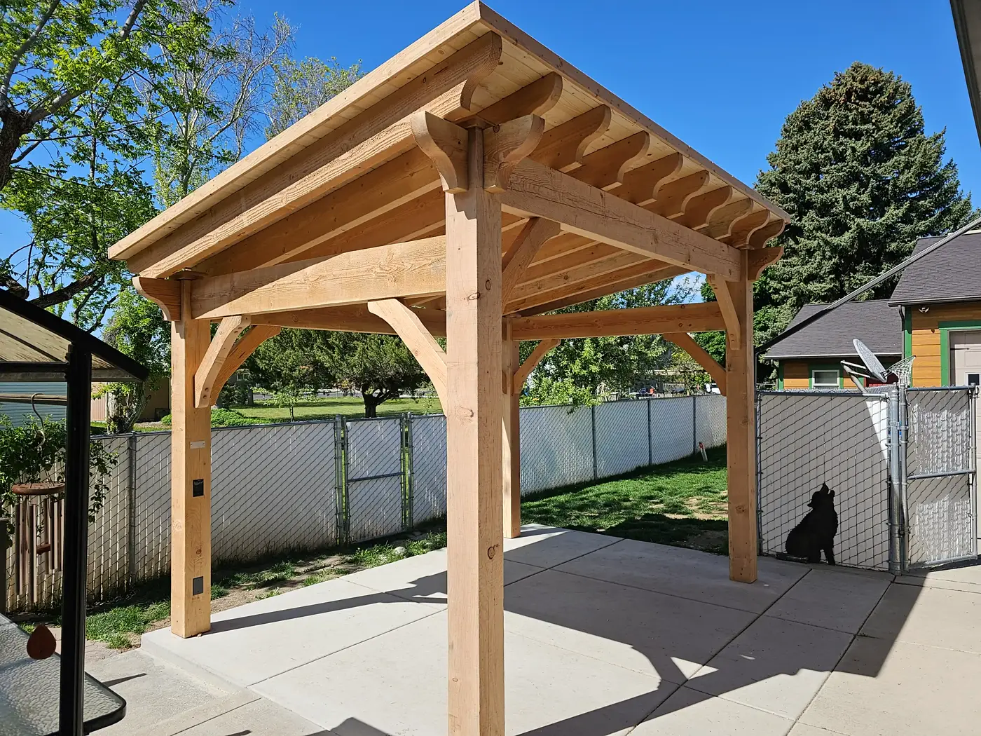 Natural cedar timber pavilion with curved braces on a concrete patio
