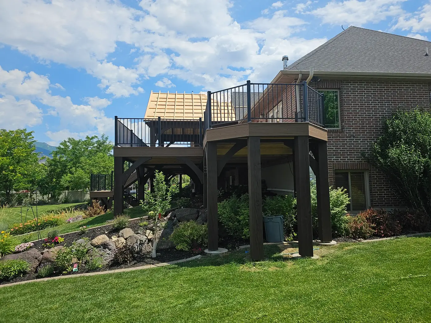 Wide view of an elevated composite deck and gable roof framing above a rock garden