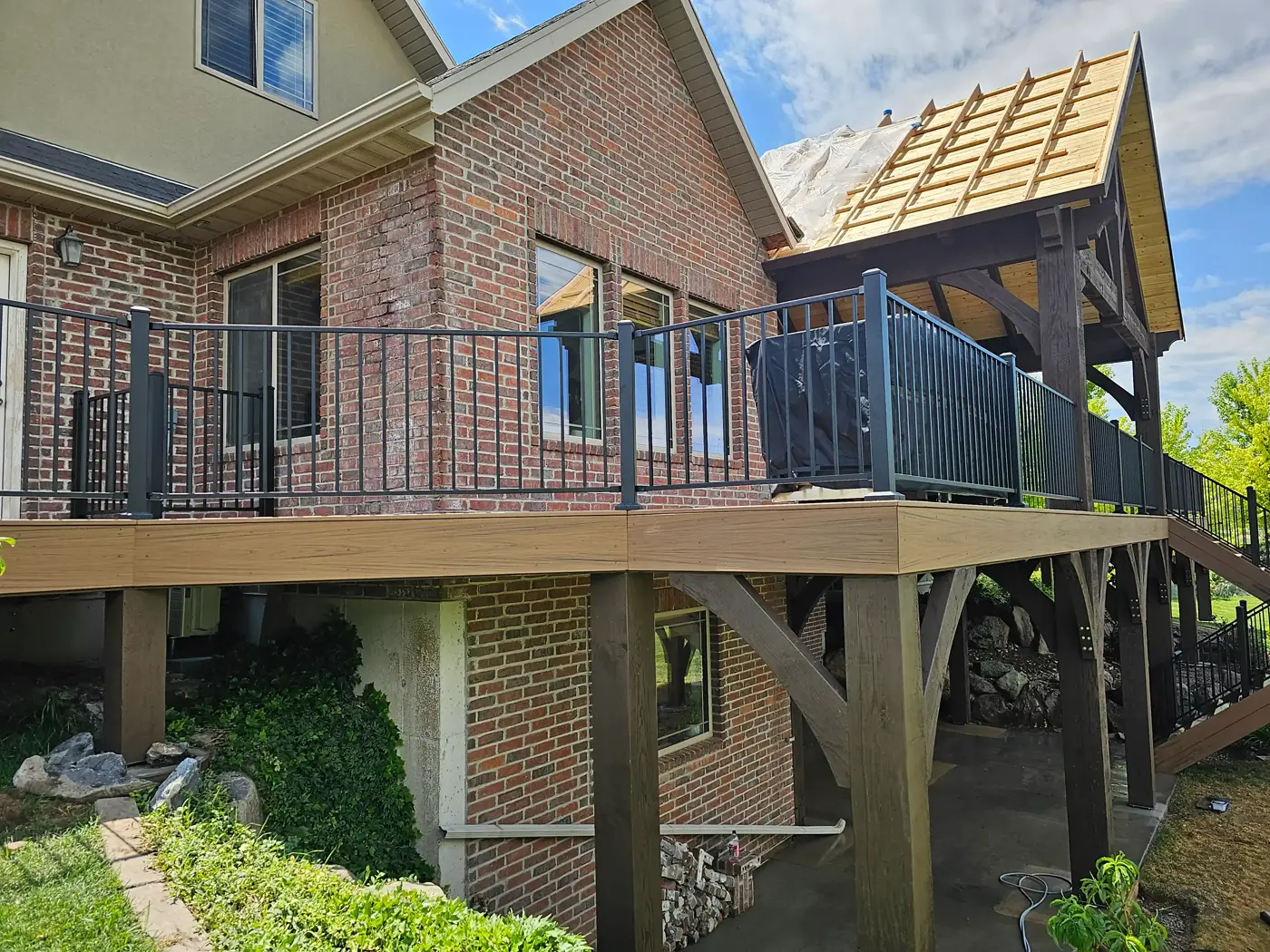 Elevated composite deck on timber posts at the back of a brick home, with roof framing above