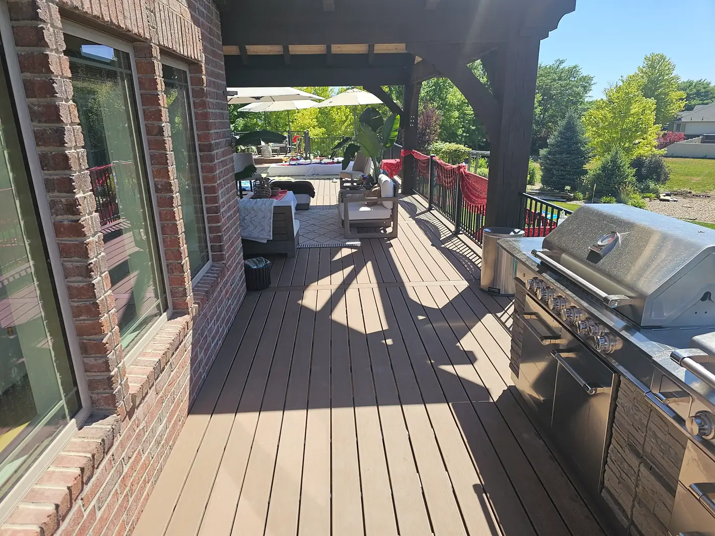 Long covered composite deck along a brick wall with a built-in outdoor kitchen grill