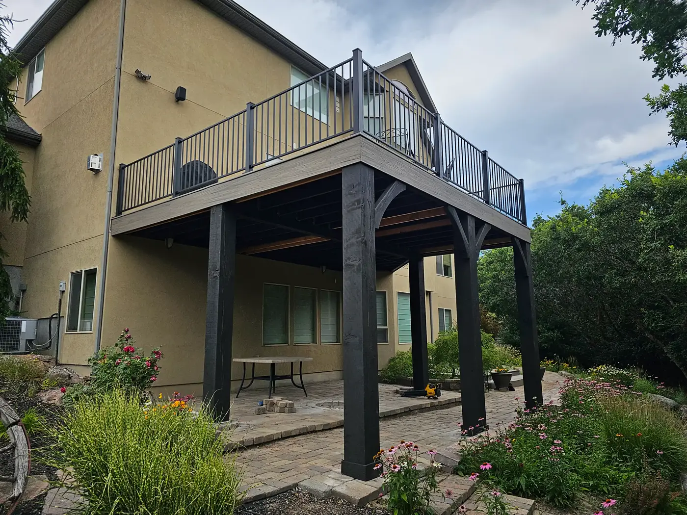 Elevated deck with black railing on tall black-stained posts over a paver patio