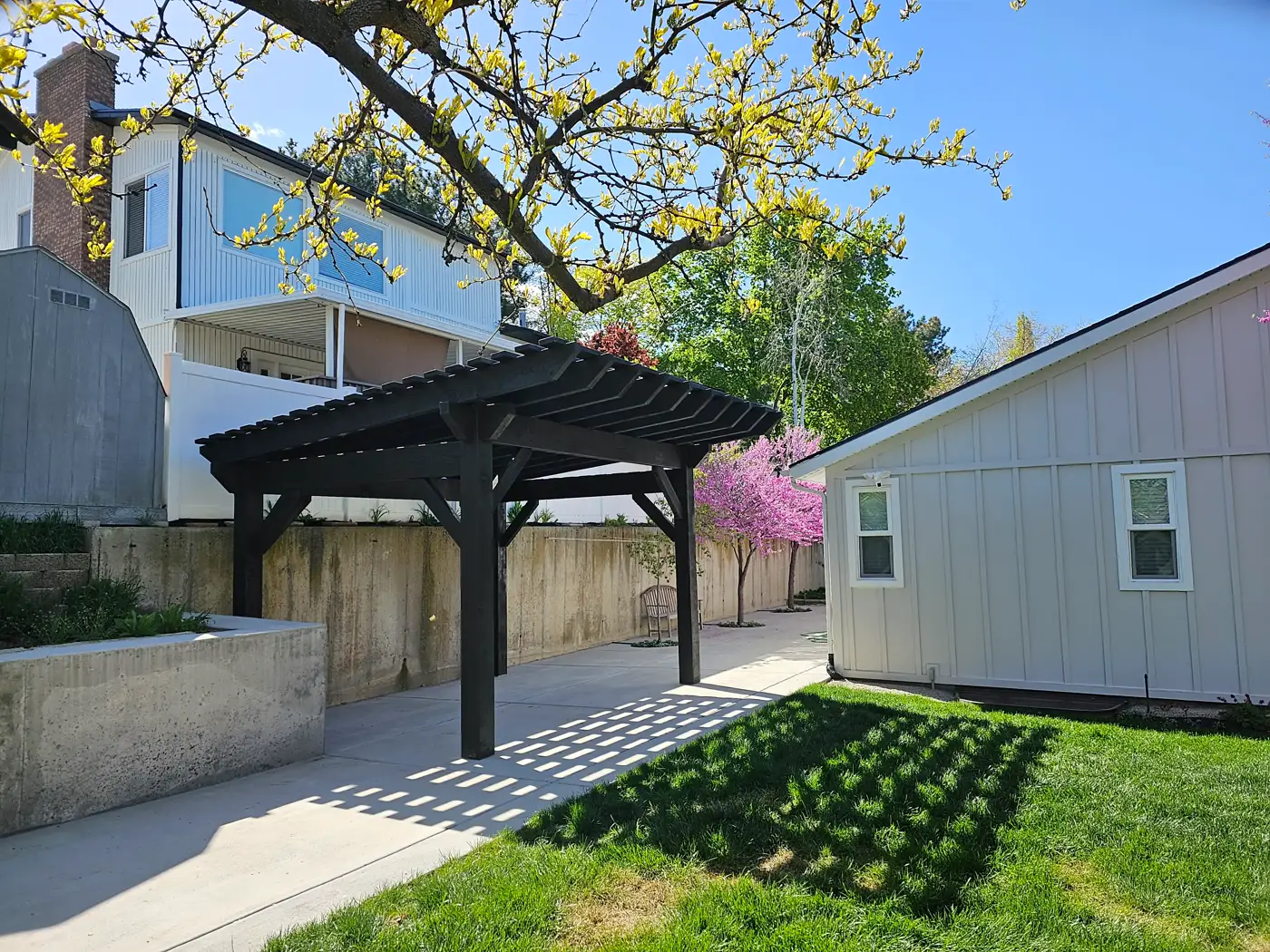 Black-stained pergola in a landscaped backyard seen from the lawn