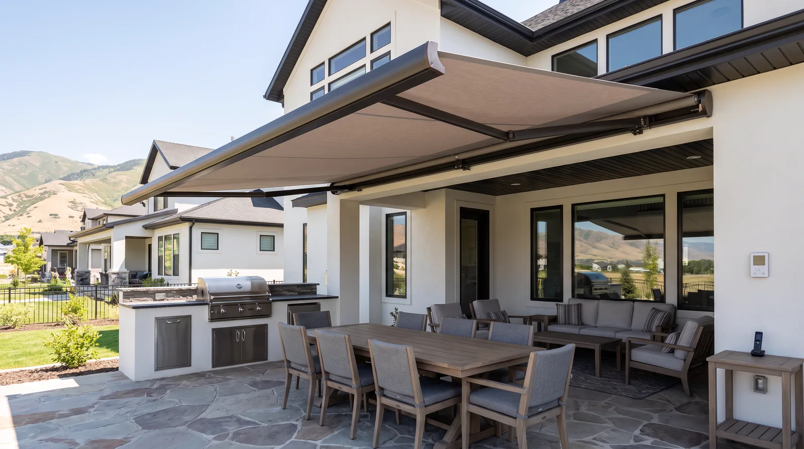 Retractable awning shading a patio with an outdoor kitchen and dining set at a stucco home