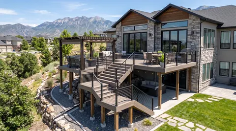 Multi-level deck with stairs stepping down a landscaped hillside behind a stone and timber home