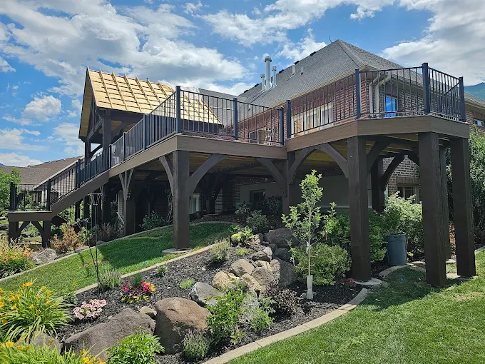 Elevated stained deck with black railing on large timber posts above a landscaped rock garden slope