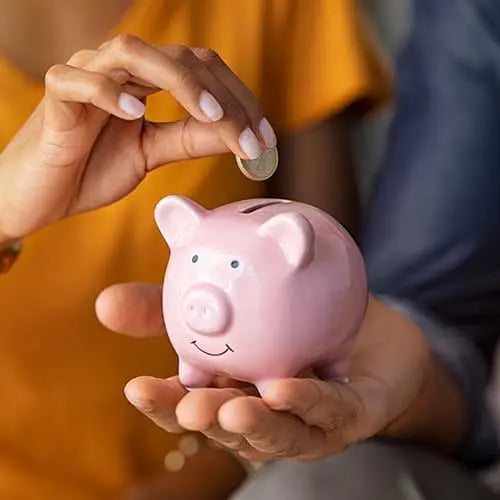 Person inserting coin into pink piggy bank for saving money