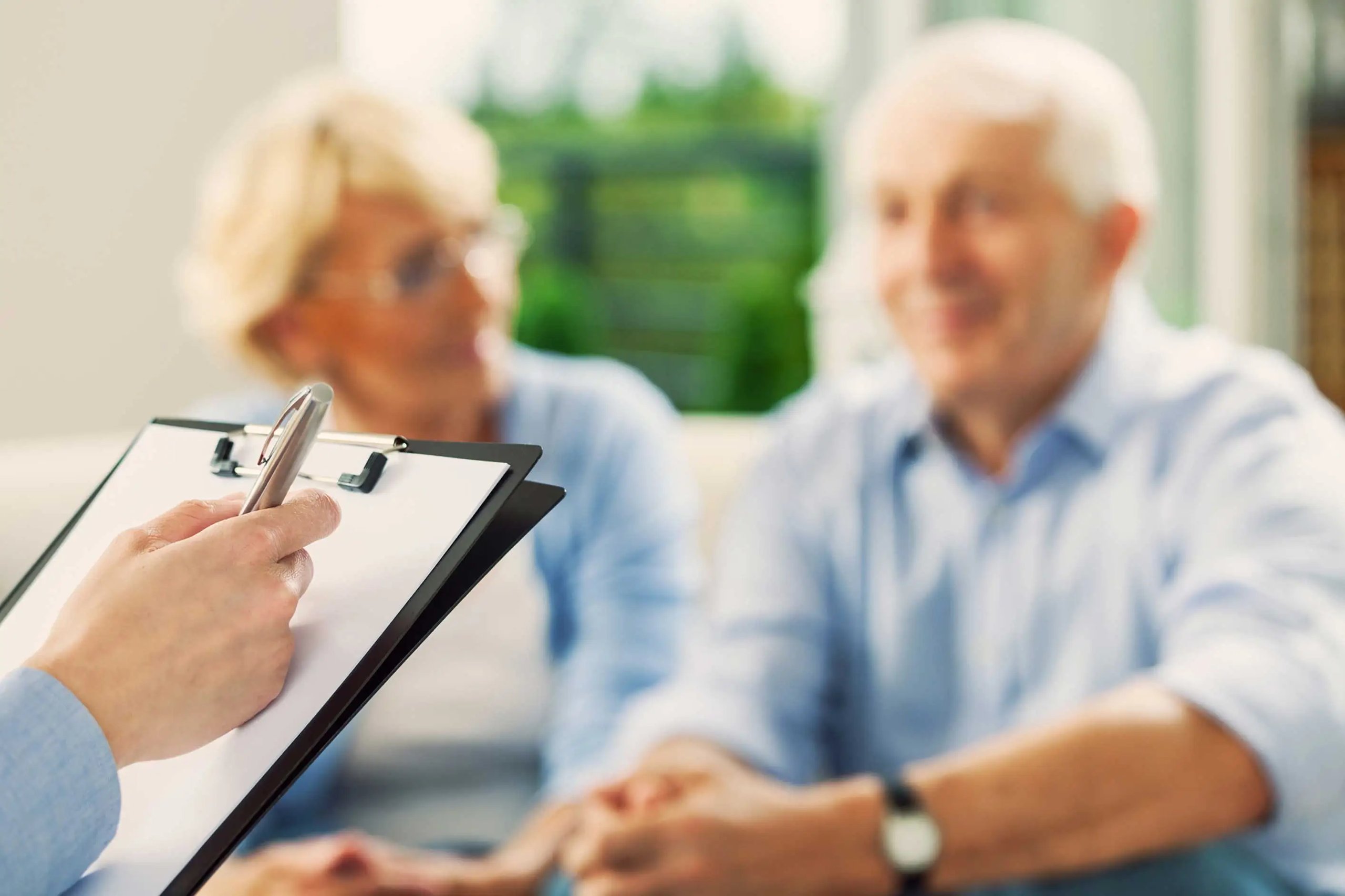 Healthcare worker holds clipboard while interviewing senior couple during medical consultation appointment