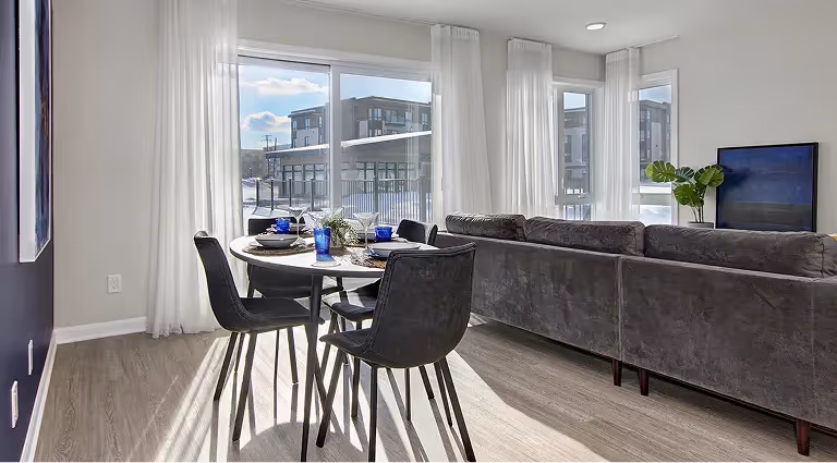 Séjour avec salle à manger, canapé gris et grandes fenêtres donnant sur l'extérieur