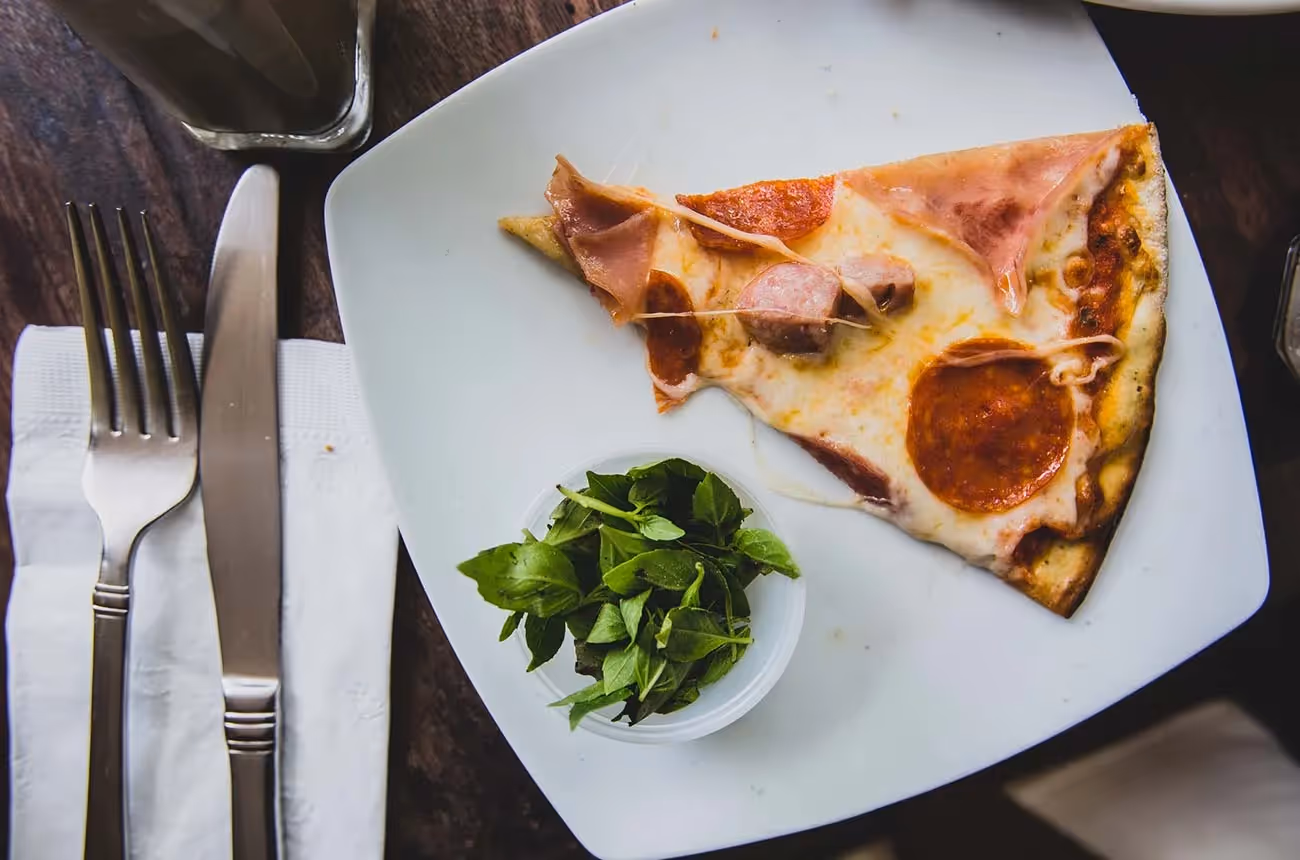 Part de pizza charcuterie servie avec salade verte sur une assiette blanche
