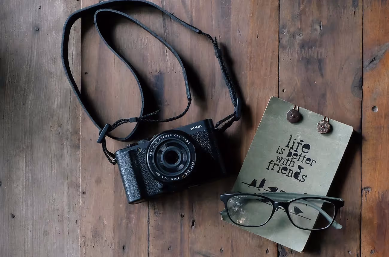 Appareil photo, carnet et lunettes posés sur une surface en bois