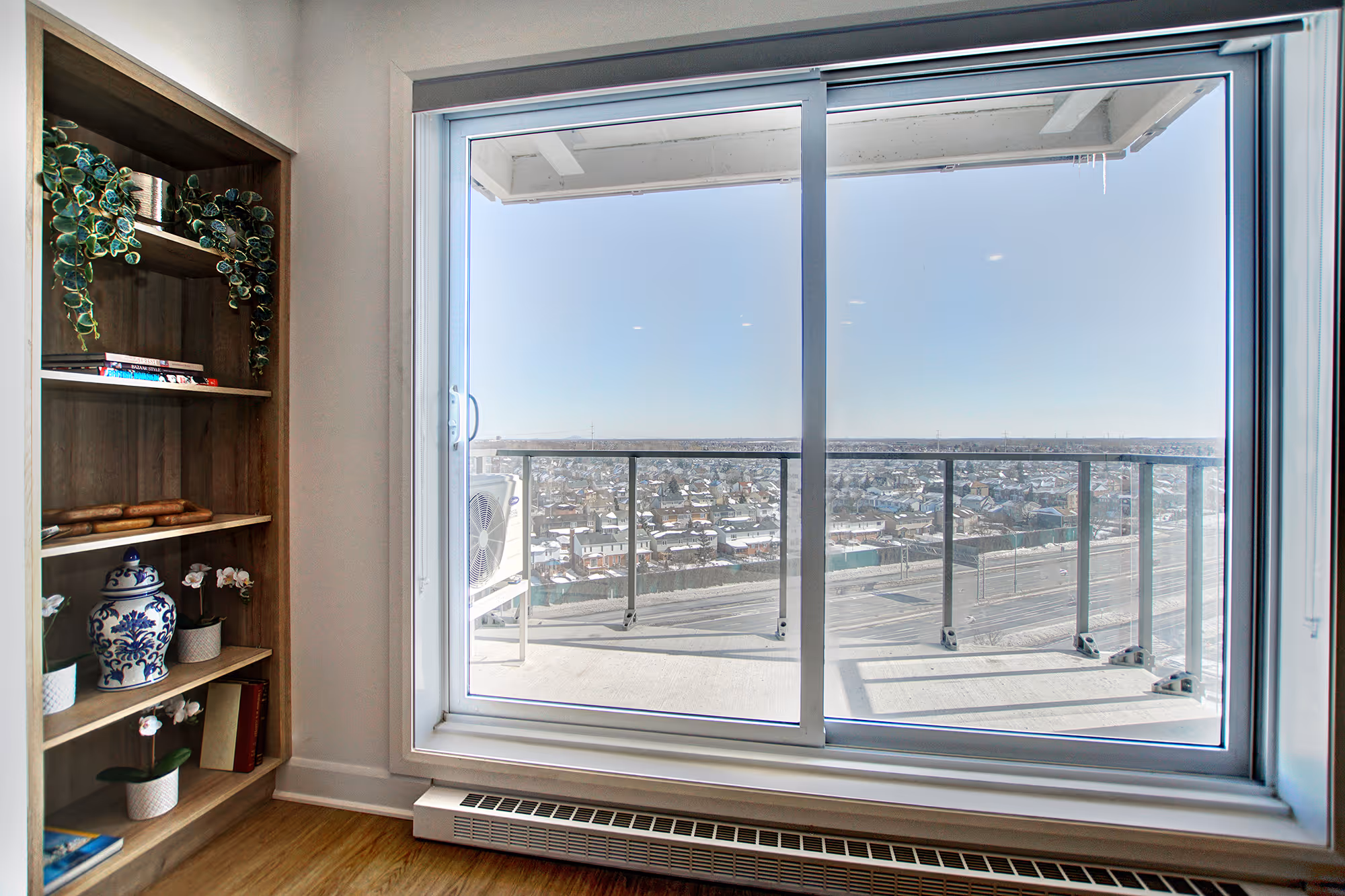 Wooden bookshelf with plants and panoramic city view from a high-rise balcony