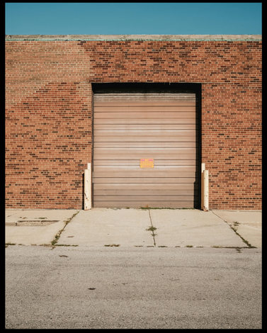 Closed beige industrial garage door in a red brick building with a concrete driveway.