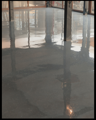 Smooth, shiny gray epoxy floor reflecting windows and structural steel beams inside a building under construction.