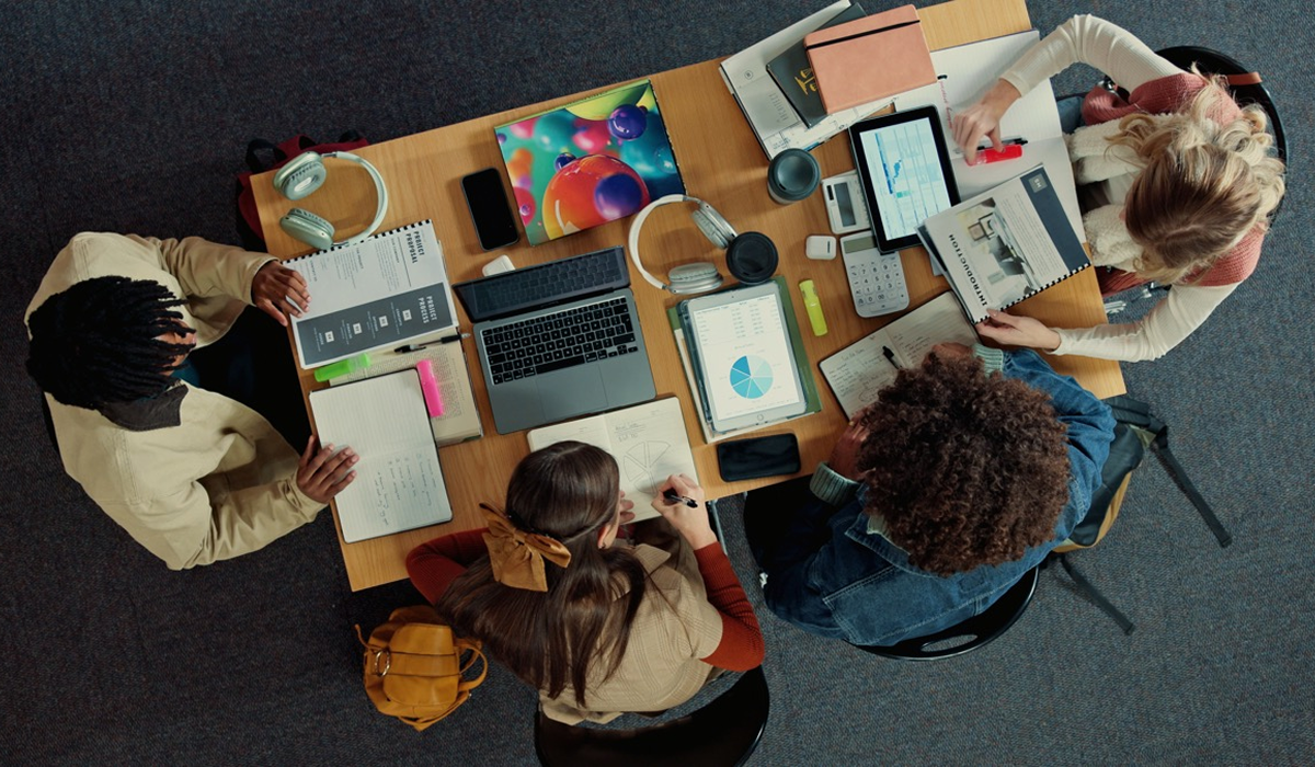 Overhead view of four colleagues reviewing documents and charts around a table with a laptop and tablets.